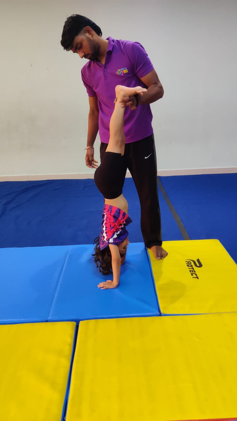 Coach supporting a child as they practise a handstand on padded mats
