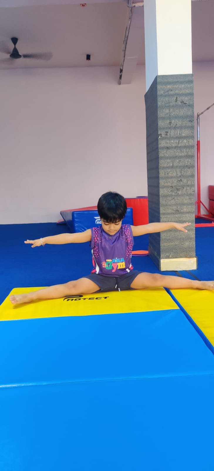 Child practising a split on a padded gymnastics mat