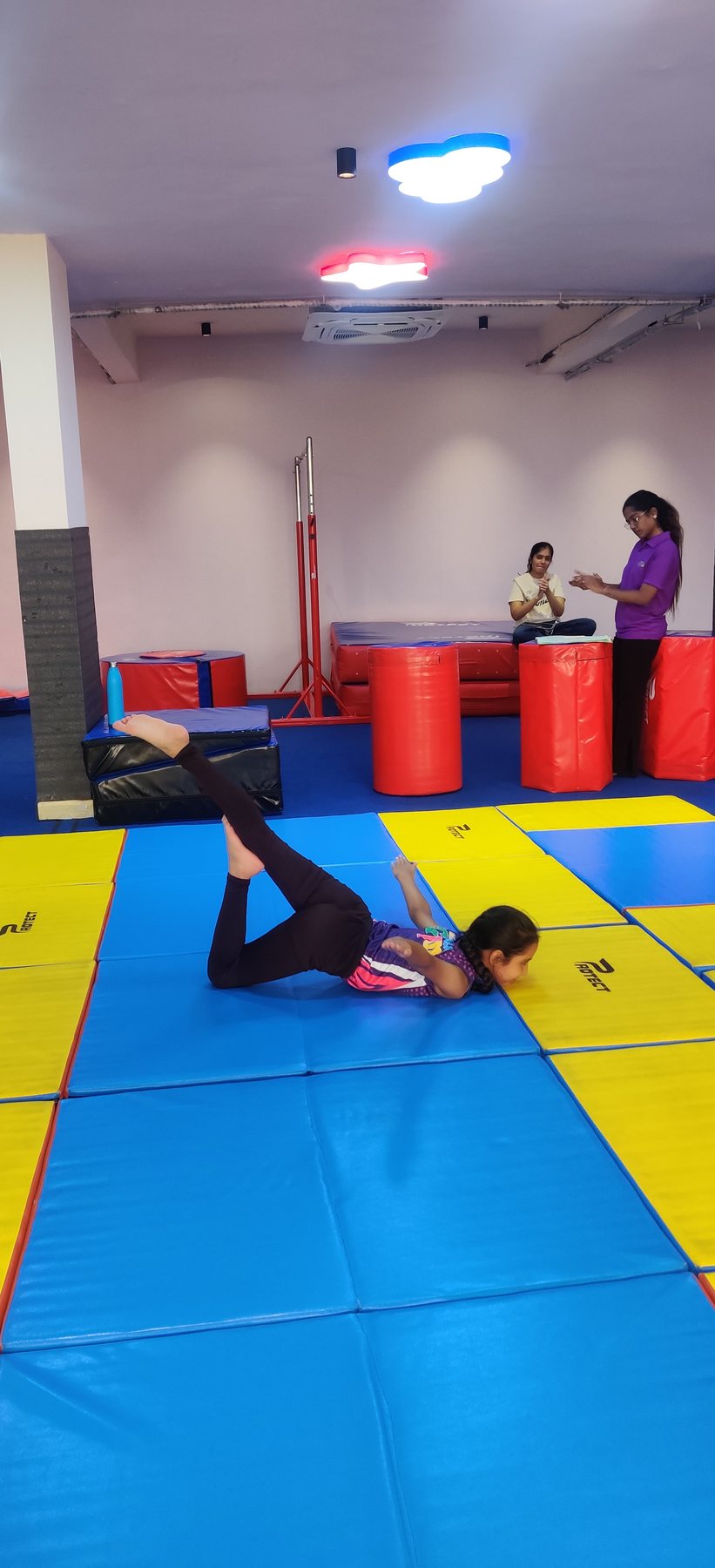 Child practising a floor movement with a coach on padded mats